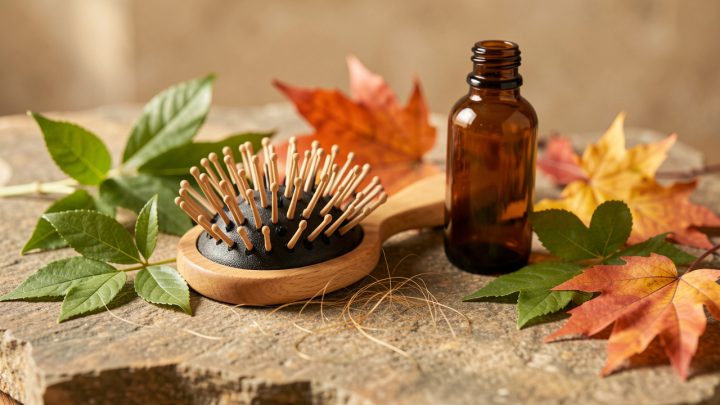 Brosse à cheveux avec quelques cheveux détachés, flacons ambrés et feuilles d’automne dans une ambiance naturelle évoquant les soins du cuir chevelu.